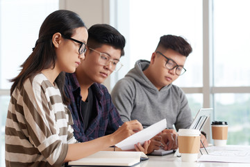 Asian students in glasses discussing document in class
