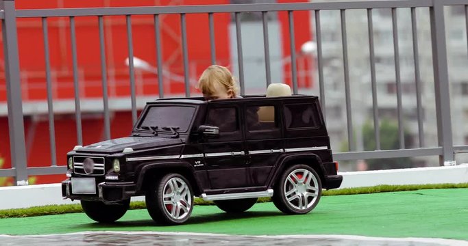 Two-year old boy riding a SUV toy car around in the city