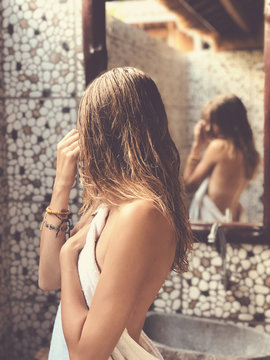 Beautiful woman touching wet hair while looking in the mirror in bathroom.