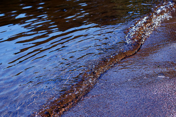 Wet sand and small wave on sandy beach. Close up horizontal image.