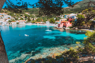 Assos village, Kefalonia, Greece. View on tourquise transparent water framed between green pine grove branches. Deep dark pattern on lagoon bottom