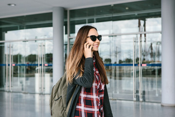 Young beautiful tourist girl at the airport or near the shopping center or the station calls a taxi or talking on a cell phone or talking to friends using a mobile phone.