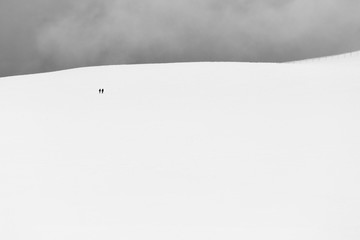 A very minimalistic view of two distant people over a mountain covered by snow