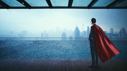Businessman in suit and cape hero stand at  swimming pool on roof top with beautiful city skyline...