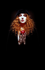 beautiful woman in black hooded cloak with long curly red hair holding an apple