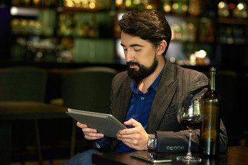 Handsome elegant man enjoying red wine and watching something on tablet computer