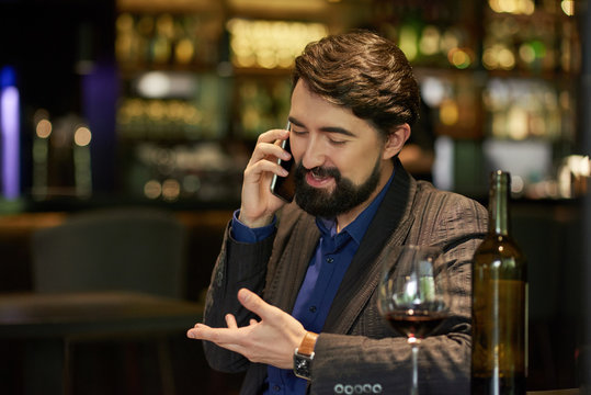 Cheerful man drinking wine in restaurant and calling on phone