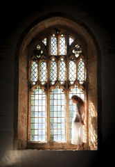 Fototapeta premium Beautiful model with long red hair posing in a Gothic window