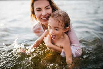 Fototapeta premium happy mother holding daughter in river and looking at camera