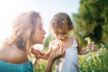 adorable daughter sniffing flowers from mom hands in field