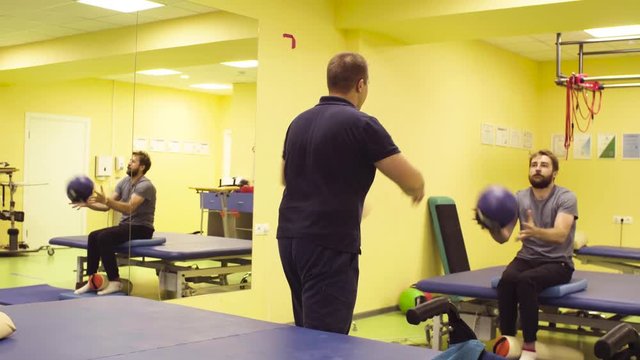 Young disabled sportsmanman doing hand exercises at the rehabilitation center with a ball. Recovery gymnastics. Active people.