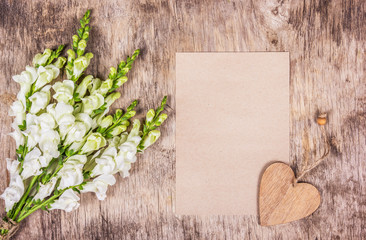 Fototapeta na wymiar Bouquet of white flowers and romantic letter. Romantic set on old wooden background. Wooden heart and tender flowers.