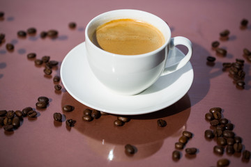 Cup of coffee with coffee beans on brown background