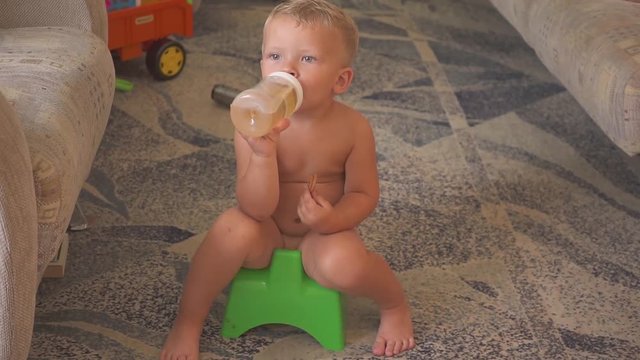 Cute boy siting on a pot at home, watching cartoons on the TV. eating and drinking.