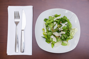 Green herb salad with shaved parmesan on a white plate.