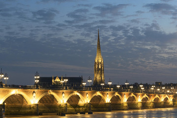 Fototapeta na wymiar Pont de Pierre stone bridge on the river garonne in Bordeaux, France at sunset with the st michel church in the background
