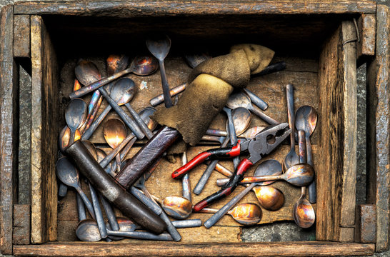 Work in process of handmade broze cutlery of spoons, forks, with iron hammer and pliers in wooden box in bronze cutlery factory, image for industrial background