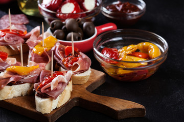 Spanish tapas with slices jamon serrano and grilled pepper. Also olives, salami, pickled onions, and peppers stuffed with cheese
