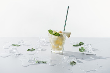 delicious summer drink with mint and melon in glass and melted ice cubes on white