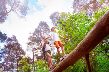 Boy and girl walks over the high log in forest
