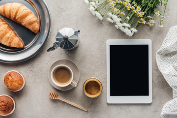 top view of coffee with pastry and tablet with blank screen on concrete surface