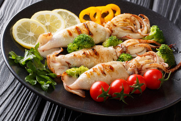 Delicious grilled squid with tentacles with tomatoes, broccoli, lemon and pepper closeup on a plate on a table. horizontal