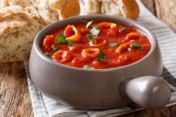 Traditional Mediterranean seafood squid rings in tomato with spices and parsley close-up in a pot and bread. horizontal