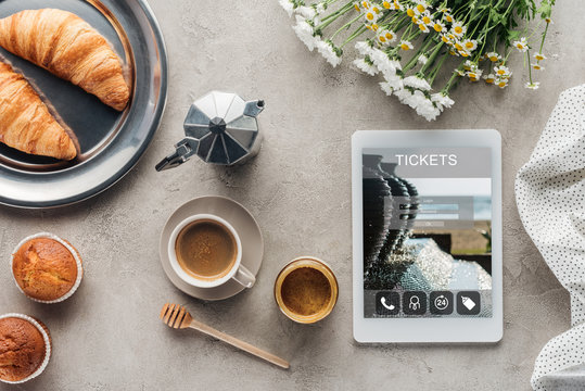 top view of coffee with pastry and tablet with tickets app on screen on concrete surface