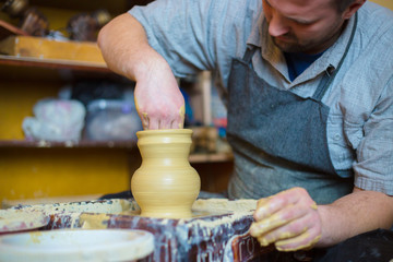 Professional male potter working with clay on potter's wheel in workshop, studio. Handmade, art and handicraft concept
