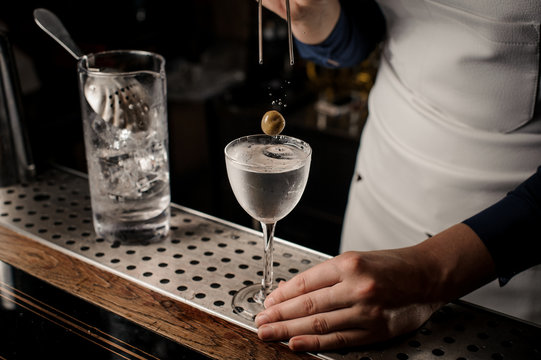 Barman hand putting an olive into an elegant cocktail glass