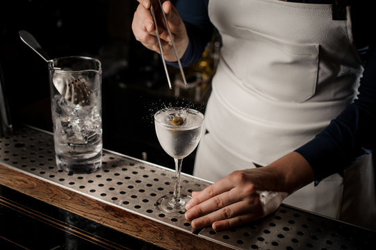 Female barman putting an olive into a cocktail glass