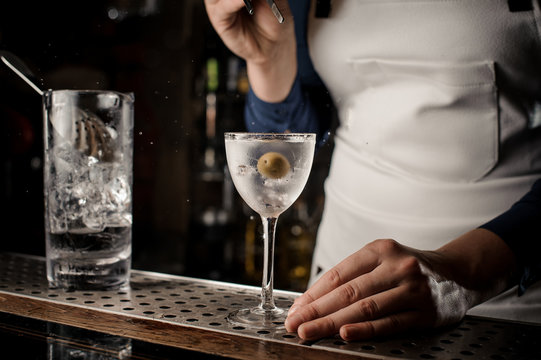 Female bartender putting an olive into a cocktail glass