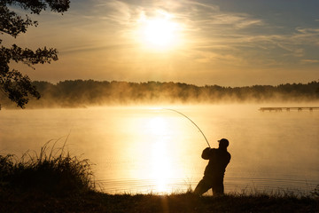 Silhouette of fisherman during foggy sunrise