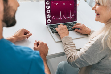 cropped shot of young man and smiling senior woman using laptop with health monitoring application...