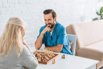 senior woman playing chess with smiling young social worker