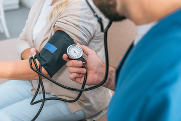 close-up partial view of caregiver measuring blood pressure to senior woman