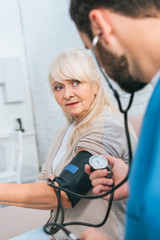 selective focus of social worker measuring blood pressure to senior woman