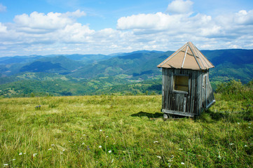 Fototapeta na wymiar abandoned wooden shed, small house, on a green meadow, blue horizon, mountains, Ukraine