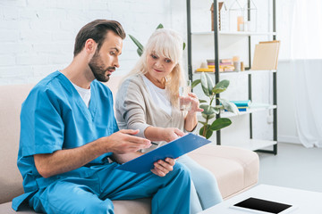 Obraz premium young male nurse showing clipboard to senior woman holding glass of water