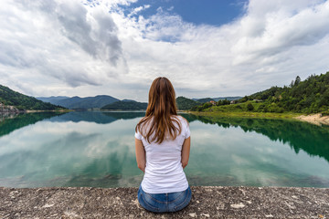 A young woman sitting and resting on Zaovine lake in Serbia. Rear view