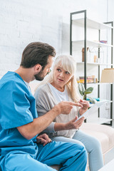 Obraz premium shocked senior woman looking at social worker pointing with finger at digital tablet