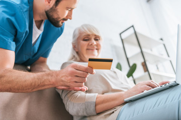 social worker holding credit card and looking at senior woman using laptop