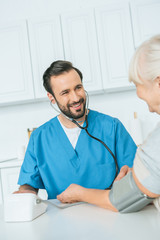 cropped shot of smiling male nurse measuring blood pressure to senior woman