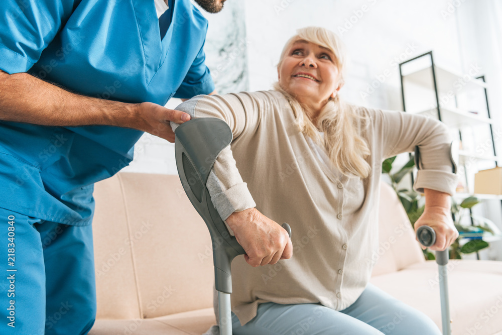 Wall mural cropped shot of social worker helping senior woman with crutches