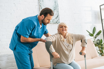 Fototapeta premium young male nurse supporting senior woman with crutches