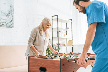 smiling senior woman and young social worker playing table football together
