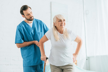 male nurse supporting senior woman with walking cane