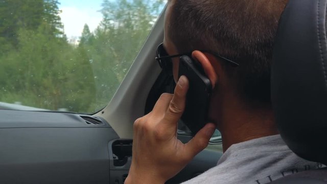 View from the back seat of a car on a young man talking on a mobile phone. Mountain countryside.