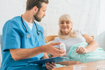 doctor holding clipboard and showing pills to senior woman lying in bed