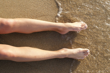 Female legs on sand washed with sea